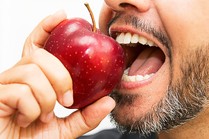 A man with a beard and black shirt holds an apple, possibly considering its impact on his root canal.